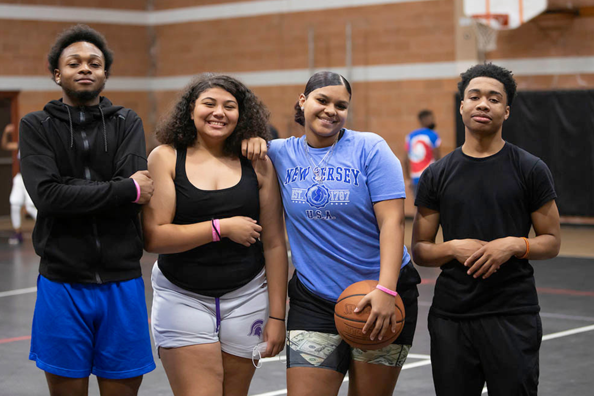 Four teenagers posing for a picture, one holding a basketball by their side