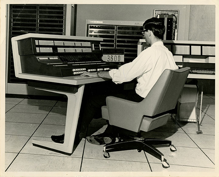 black and white photo scan, a person using a table-sized computer terminal with big switches