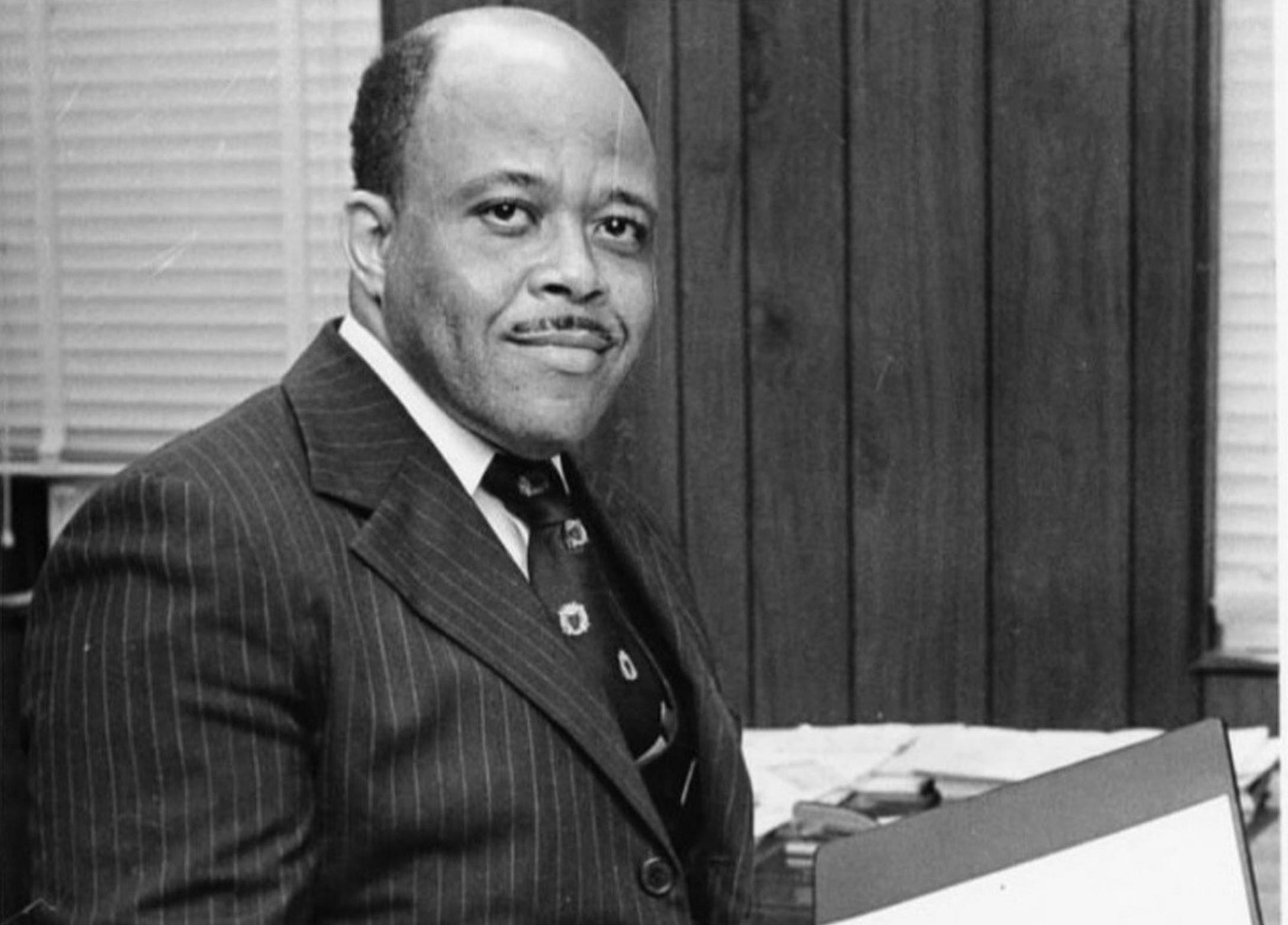 Man in suit standing in office smiling at camera.